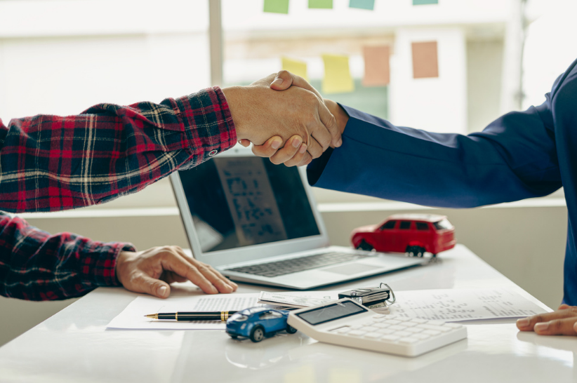 Two men shaking hands over a set of car keys and a calculator.