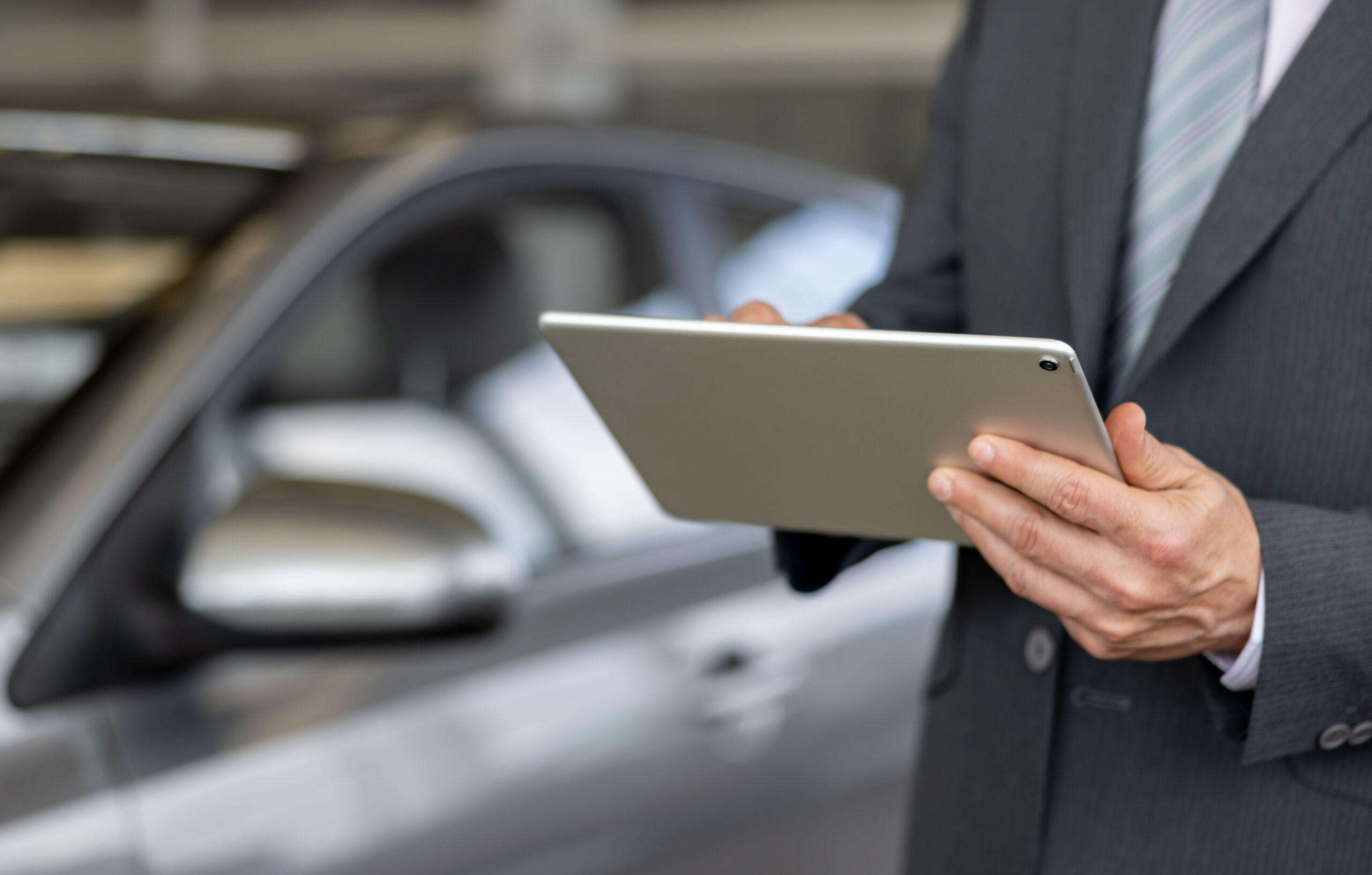 Close-up on a car salesperson using a tablet computer at the car dealership