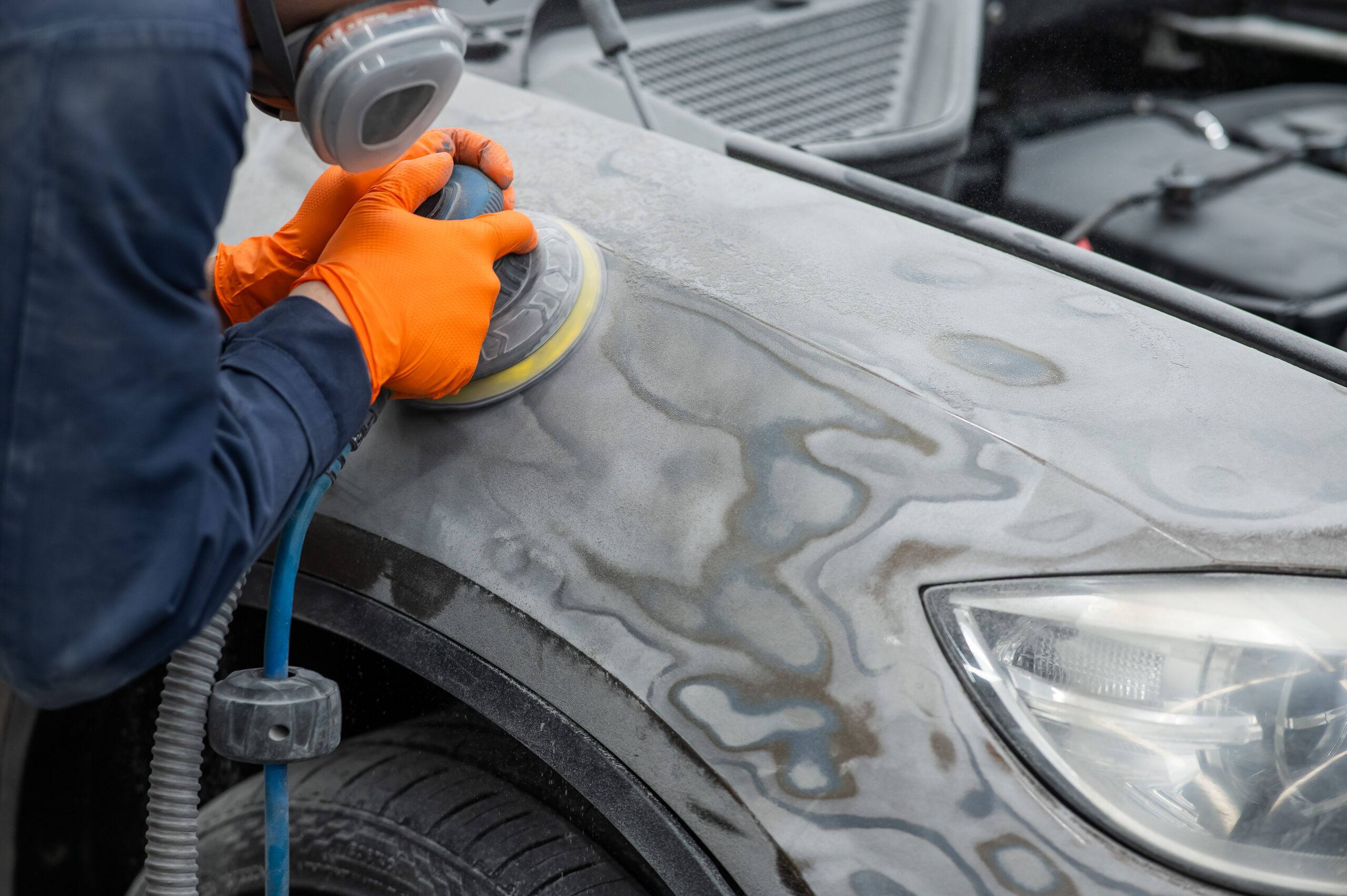 A mechanic sanding the putty on a car body with a machine.